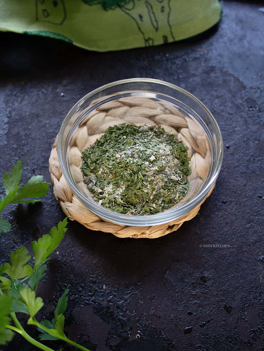 Homemade garlic herb seasoning in a glass jar with dried herbs and garlic.
